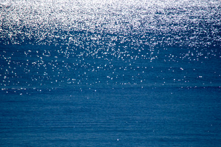Abstract background. Spots of white reflections of shining sun on blue surface of sea waves. Sea on sunny day. Natural bokeh texture backdrop. Seamless looping. Beautiful natural backgroundの写真素材