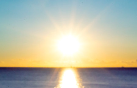Blurred background. Sun shining in blue sky during sunset dawn. Sunrise dawning sundown. Sunny path, sunny walkway on surface of sea waves. Sunlight Sunbeams Sea landscape Natural blurry bokeh textureの写真素材
