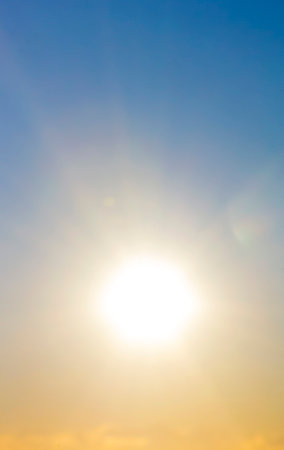 Blurred background. Sun in sky. Bright sun with sunbeams shines on clean yellow blue sky. Bright sun light, sun ray lens flares, sunshine day, sunny light, sunshiny boke. Beautiful natural backgroundの写真素材