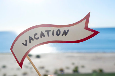 Stick with paper speech bubble with words Vacation on background sea, sky, sandy beach on a sunny summer day. Text-balloons with text from letters. Concept, symbol, sign vacation travel tourism rest.の写真素材