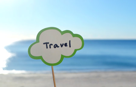Stick with paper speech bubble with words Travel on background blue sea, sky, sandy beach on sunny summer day. Text-balloons with text from letters. Concept, symbol, sign vacation travel tourism restの写真素材