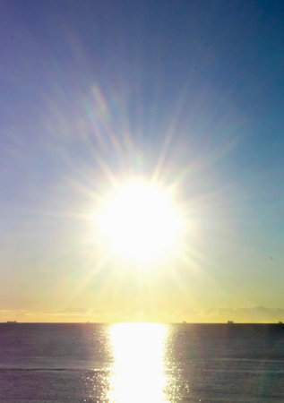 Blurred background. Sun shining in blue sky during sunset dawn. Sunrise dawning sundown. Sunny path, sunny walkway on surface of sea waves. Sunlight Sunbeams Sea landscape Natural blurry bokeh textureの写真素材