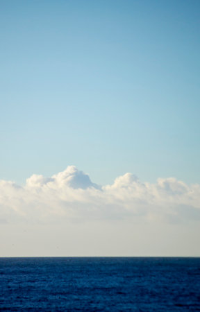 White cumulus clouds over the blue surface of the sea on sunny day. Beautiful natural background. Movement of clouds in the sky. Sky landscape. Seascape. White blue colors. Place for text, copy spaceの写真素材