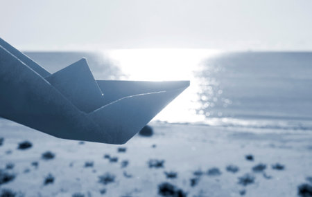 A person playing with paper boat on background of sky, sandy beach and sea with sunny path on sunny summer day. Concept travel tourism holidays vacation dream childhood game fantasize. Blue colorの写真素材