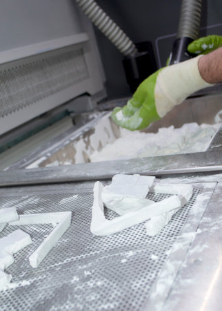 Male worker taking out models from white polyamide powder in working chamber of 3D printer, cleaning powder and putting on surface. Process of creating model on powder 3D printer. Multi Jet Fusion MJFの写真素材