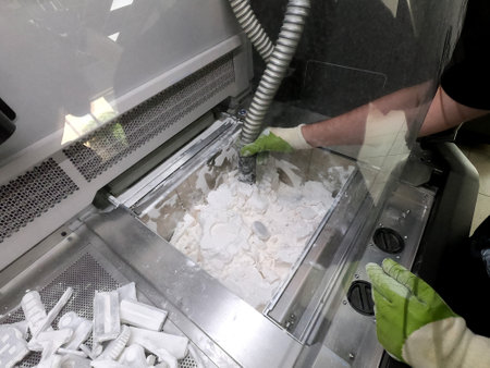 Male worker taking out models from white polyamide powder in working chamber of 3D printer, cleaning powder and putting on surface. Process of creating model on powder 3D printer. Multi Jet Fusion MJFの写真素材