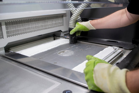 A male worker cleans the surface of an industrial 3D printer from white powder with a vacuum cleaner close-up. Multi Jet Fusion MJF 3D printing. The working process. 3d printing technologyの写真素材