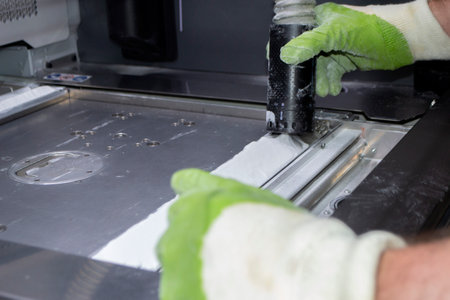 A male worker cleans the surface of an industrial 3D printer from white powder with a vacuum cleaner close-up. Multi Jet Fusion MJF 3D printing. The working process. 3d printing technologyの写真素材