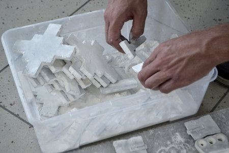 Male worker sorts through models in hands, lying in box and covered with white polyamide powder close-up. Objects printed on powder 3D printer. Technology Multi Jet Fusion MJF. 3D printing technologyの写真素材