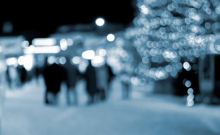 Blurred background. Christmas tree, decorated glowing lights, building silhouettes of people walking city square at winter night. Beautiful New Year and Christmas holiday blurred background Blue colorの写真素材