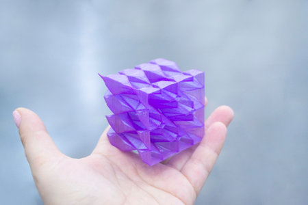 Person holding a abstract model printed on a 3D printer from purple plastic on his hand on gray background close-up. Concept modern printing technologyの写真素材