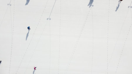 People ride on white ice rink on street and cast long shadows. People skating on sunny winter day. Top view. Aerial drone view. Leisure entertainment vacation weekend holidays activities lifestyle.の写真素材