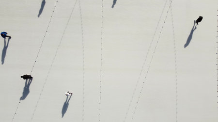 People ride on white ice rink on street and cast long shadows. People skating on sunny winter day. Top view. Aerial drone view. Leisure entertainment vacation weekend holidays activities lifestyle.の写真素材