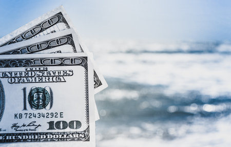 Girl holding money bill of 300 dollars on background of sea ocean waves and blue sky close-up. Hand wave sea ocean money dollars vacation. Concept finance money holiday travelingの写真素材