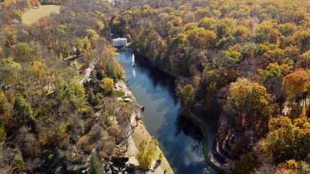 Beautiful panoramic autumn landscape park, many trees with yellow leaves, lake with fountain in center, architecture, big stones, paths walkways, people walking on sunny autumn day. aerial drone viewの写真素材