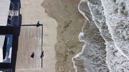 People sitting on a sandy beach near the sea and sea waves with white foam. People rest and relaxing near the sea. Flying over a sandy beach with people on a sunny day. Top view. Aerial drone viewの写真素材