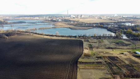 Urban beautiful landscape agricultural plowed fields, lakes for growing fish, gardens, thermal power plant, building industrial area of city, cloud shadows on sunny autumn day. Aerial drone view.の写真素材