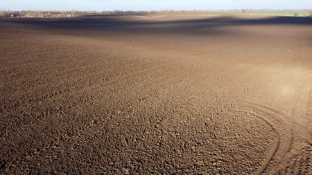 Landscape of plowed up land on agricultural field with cloud shadows on sunny autumn day. Flying over plowed earth with black soil. Agrarian background. Ground earth dirt priming. Aerial drone view.の写真素材