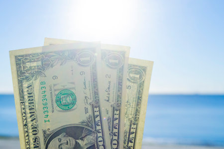 Three denominations of US dollars banknotes with face value of one dollar on background of sea waves on sandy beach of the seashore on a sunny summer day. Concept money financeの写真素材
