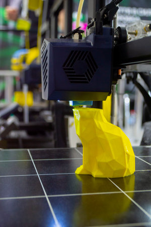 3D printer printing prototype of toy from molten plastic. Process of creating prototype model of toy on 3D printer from yellow melted plastic close-up. Additive new printer technology. Modern printingの写真素材