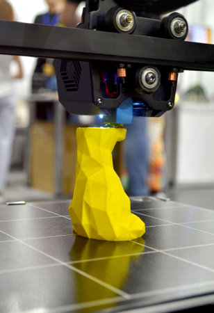 3D printer printing prototype of toy from molten plastic. Process of creating prototype model of toy on 3D printer from yellow melted plastic close-up. Additive new printer technology. Modern printingの写真素材