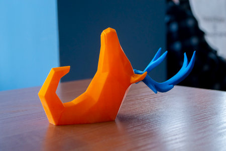 Art object printed on 3D printer. Abstract toy model orange deer with blue horns lying on the table and created on 3d printer. FDM. Concept 3D Printing. Additive modern new progressive technologiesの写真素材