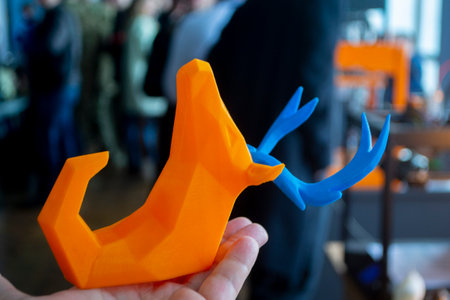 Person holding in hand an art object printed on 3D printer. Abstract toy model orange deer with blue horns created on 3d printer. FDM. Concept 3D Printing. Additive modern new progressive technologiesの写真素材