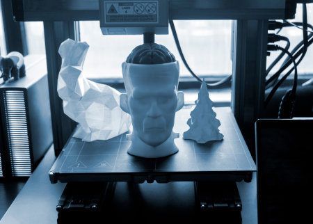 Art models printed on 3D printer on desktop of 3D printer. Models of prototype human head with brain, figured hare and Christmas tree printed on 3D printer from molten plastic of different colorsの写真素材