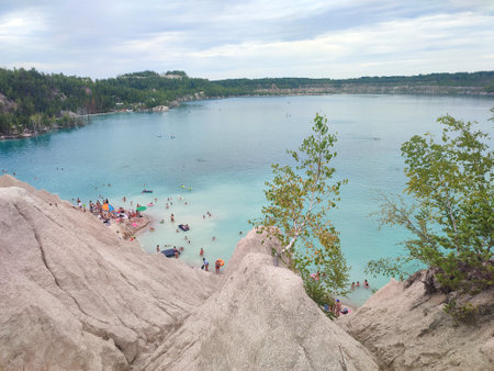 Many people swimming in the blue water near the sandy shore in a flooded quarry on a summer day. Beautiful blue water of large lake and many people swimming near the sandy shore of the slope. Top viewの写真素材