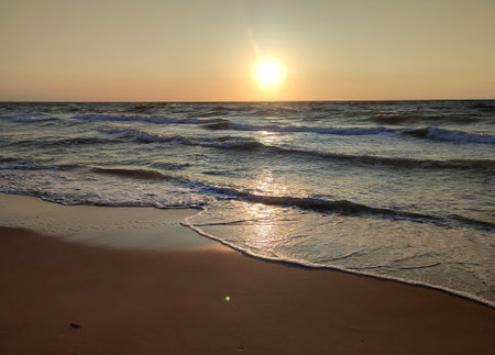 Stormy sea. Big waves with white foam on sea on backdrop of sunset and dawn. Blue sea, orange red sky, sun. Coast seashore seaside shore coastline. Natural background nature backdrop stormの写真素材