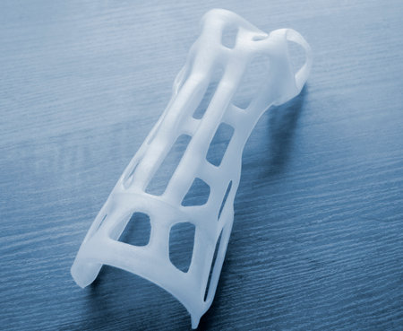 Hand splint corset prosthesis printed on 3D printer from molten white plastic powder on table. Medical orthosis fixator plastic overlay created on 3D printer. New modern medical 3D printing technologyの写真素材