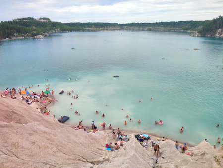 Many people swimming in the blue water near the sandy shore in a flooded quarry on a summer day. Beautiful blue water of large lake and many people swimming near the sandy shore of the slope. Top viewの写真素材