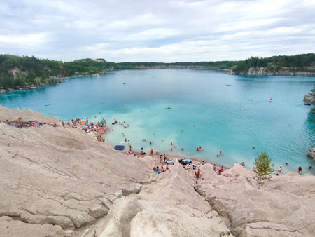 Many people swimming in the blue water near the sandy shore in a flooded quarry on a summer day. Beautiful blue water of large lake and many people swimming near the sandy shore of the slope. Top viewの写真素材