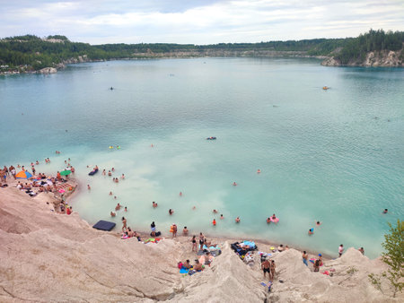 Many people swimming in the blue water near the sandy shore in a flooded quarry on a summer day. Beautiful blue water of large lake and many people swimming near the sandy shore of the slope. Top viewの写真素材