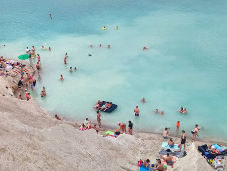 Many people swimming in the blue water near the sandy shore in a flooded quarry on a summer day. Beautiful blue water of large lake and many people swimming near the sandy shore of the slope. Top viewの写真素材