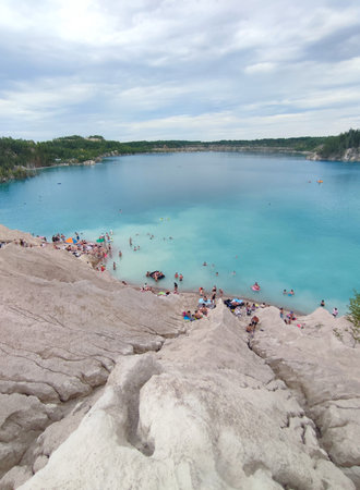 Many people swimming in the blue water near the sandy shore in a flooded quarry on a summer day. Beautiful blue water of large lake and many people swimming near the sandy shore of the slope. Top viewの写真素材