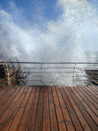 Large wave hitting wooden pier jetty with a lot of splashes on a sunny day. Stormy sea. Weather. Travel, tourism, vacation. Coast, coastal, shoreの写真素材