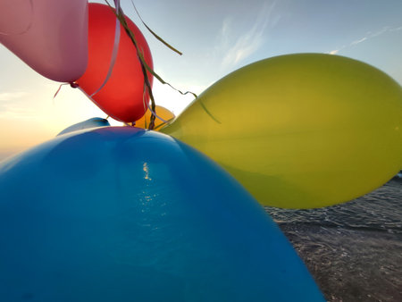 Woman playing with many colorful balloons on the sandy beach of the seashore near the sea at sunrise...