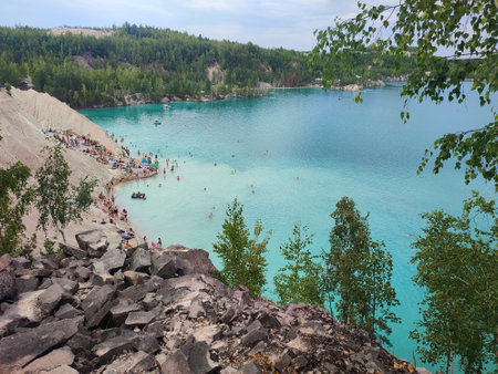 Many people swimming in the blue water near the sandy shore in a flooded quarry on a summer day....