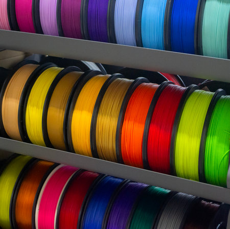 Many spools with multi-colored plastic for 3D printing. Spools with yellow, orange, brown, red green plastic wire for 3D printer. Components for 3D printing. Accessories for 3D printer. FDM technologyの写真素材