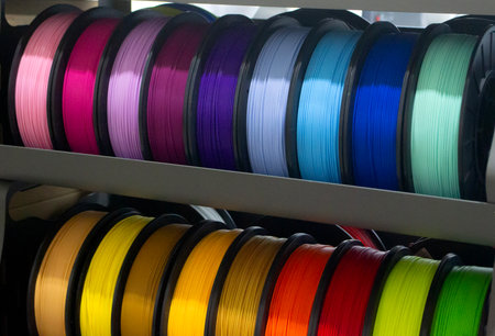 Many spools with multi-colored plastic for 3D printing. Spools with pink, red, burgundy, purple blue...