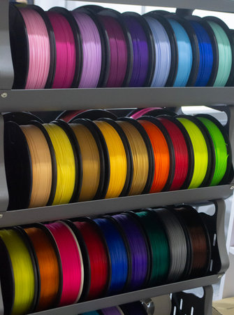 Many spools with multi-colored plastic for 3D printing. Spools with pink, red, burgundy, purple,...