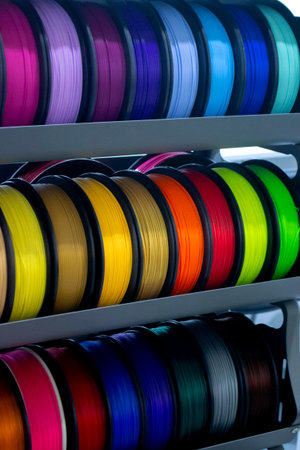 Spools with multi-colored plastic for 3D printing. Spools with pink, red, burgundy, purple, yellow, orange blue plastic wire for 3D printer. Components for 3D printing. Accessories for 3D printerの写真素材