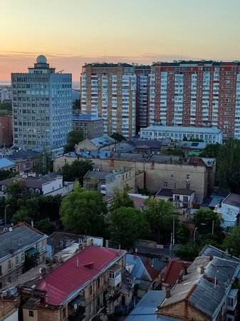 Cityscape. Old buildings with roofs, green trees, road and moving cars on sunny summer evening. Windows and walls of old houses, multi-story buildings in city. City scenery. Urban landscape.の写真素材