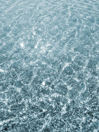 Clean transparent water on shallow sandy seashore with shells on sunny summer day. Sun glare on surface of water. Small waves on sea coast. Nature backdrop. Natural backgroundの写真素材