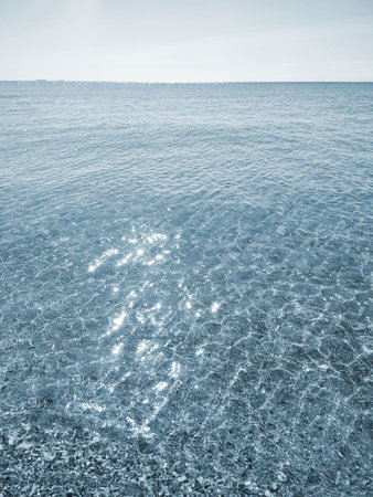 Clean transparent water on shallow sandy seashore with shells on sunny summer day. Sun glare on surface of water. Small waves on sea coast. Nature backdrop. Natural backgroundの写真素材