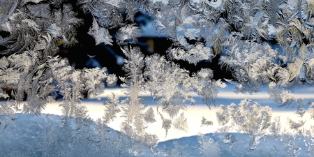A thin drawing of ice crystals on a vertical glass on a background of a winter, snowy landscape.の写真素材