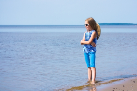 Little girl in a striped vest and hat on the beachの写真素材
