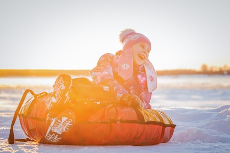 Pretty cute girl on soft sleigh laughing and looking away on the background of nature in the sunsetの写真素材