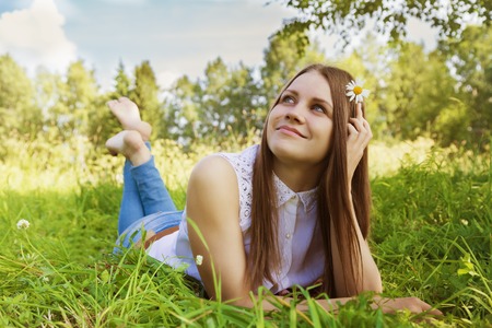 Beautiful girl lies on meadow with chamomile flowers in her hairの写真素材